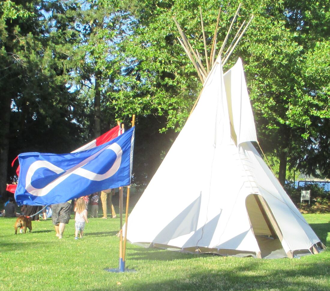 A tipi and the Métis flag at a community gathering in the park